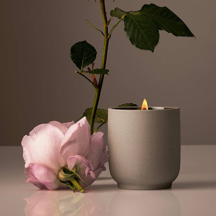 Ceramic candle holder with a lit candle and pink roses on a reflective surface.