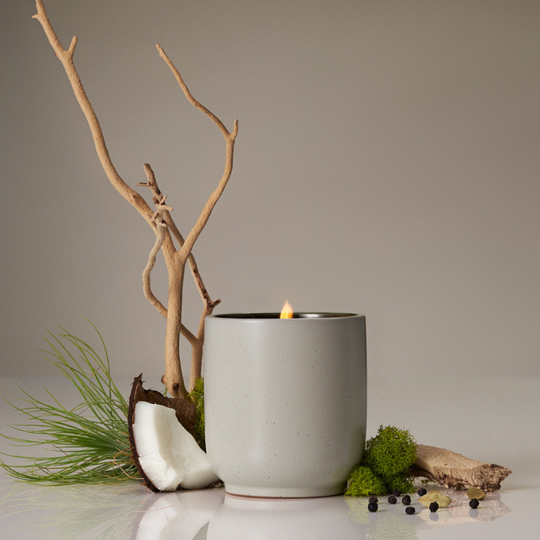Gray candle in a pot with natural elements like branches and moss on a neutral background