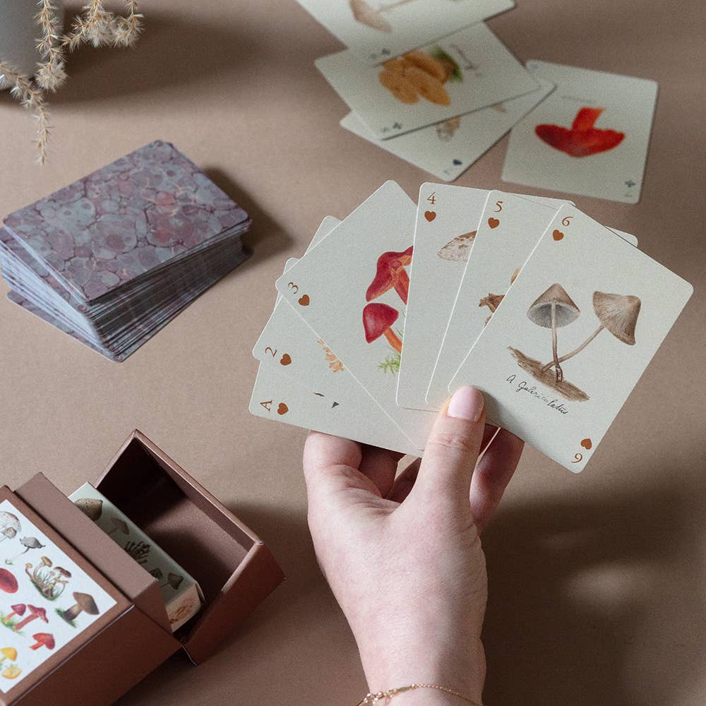 Hand holding playing cards with nature-themed designs on a brown surface
