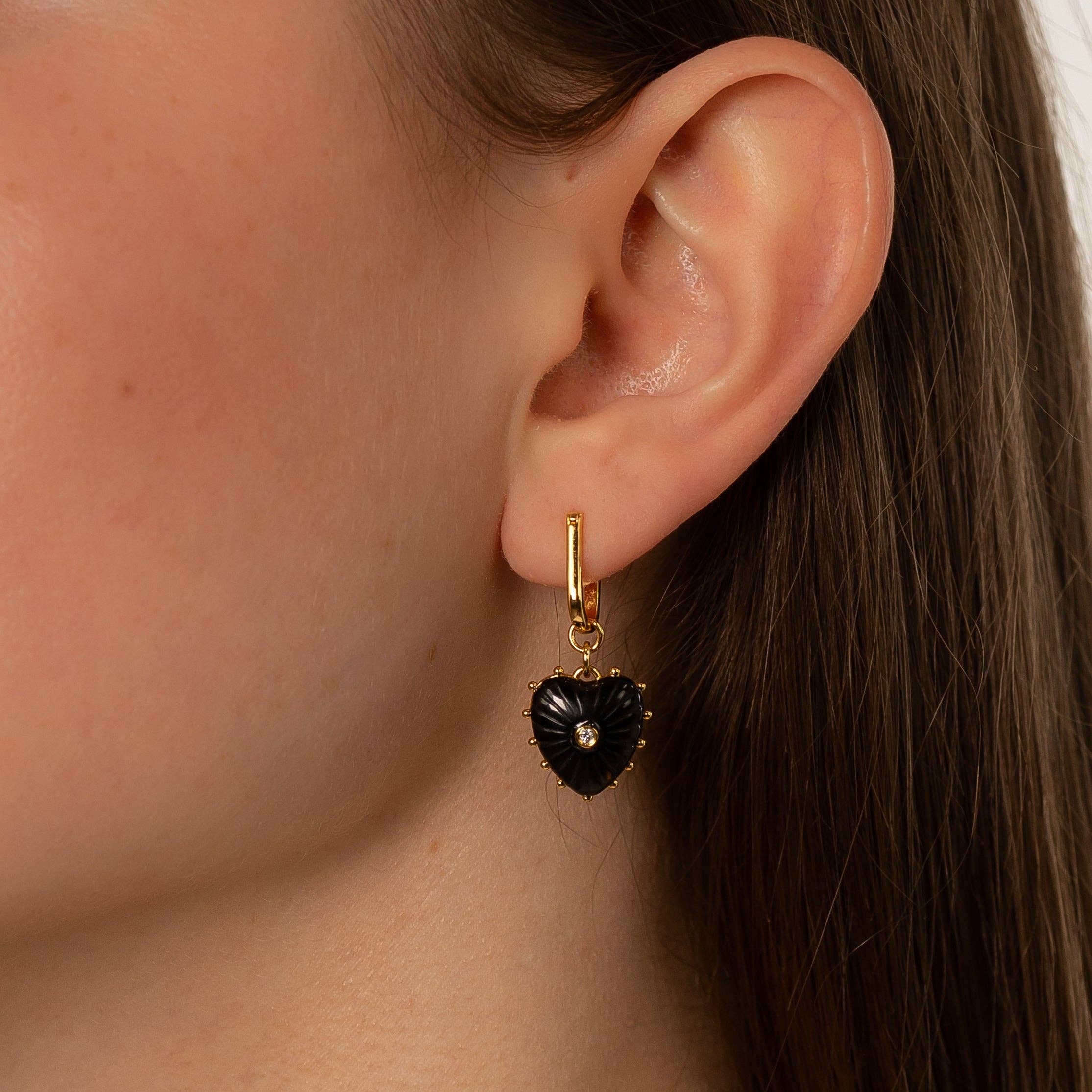 Close-up of an ear wearing a gold earring with a black heart pendant.