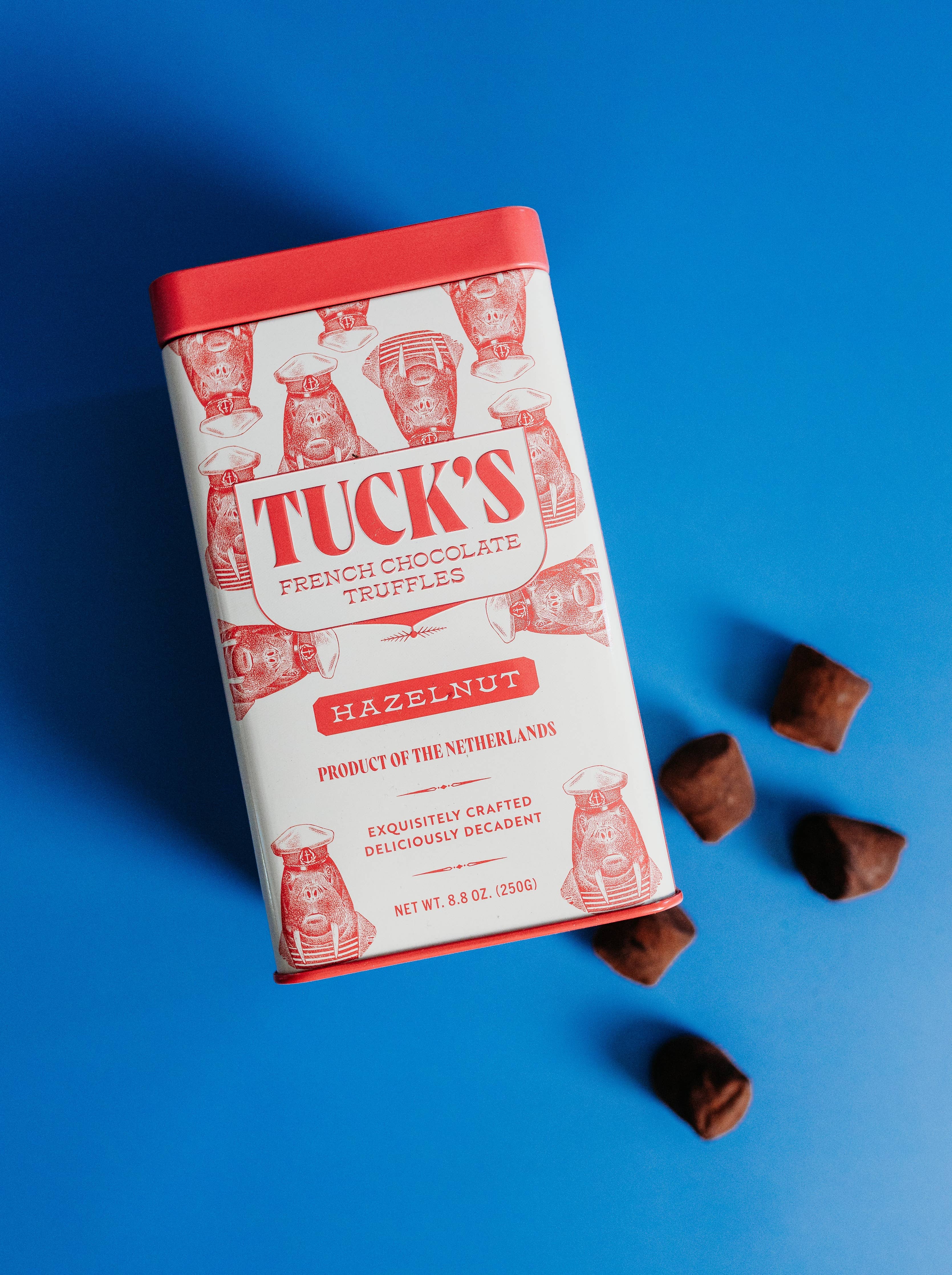 Tuck's French Chocolate Truffles hazelnut tin on a blue background with chocolate truffles around