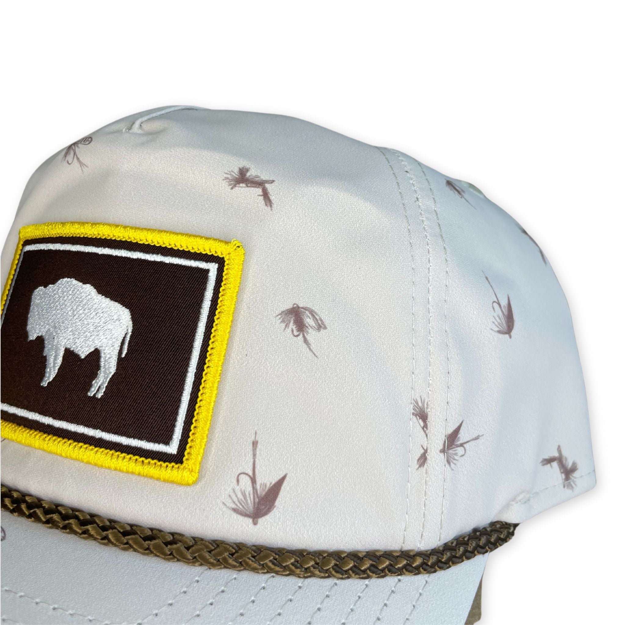 White hat with Wyoming flag patch on front. pattern of fishing lures on whole hat.