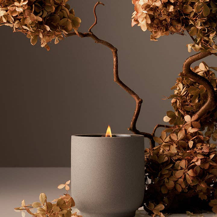 Gray candle holder with a lit candle surrounded by dried hydrangea flowers on a neutral background