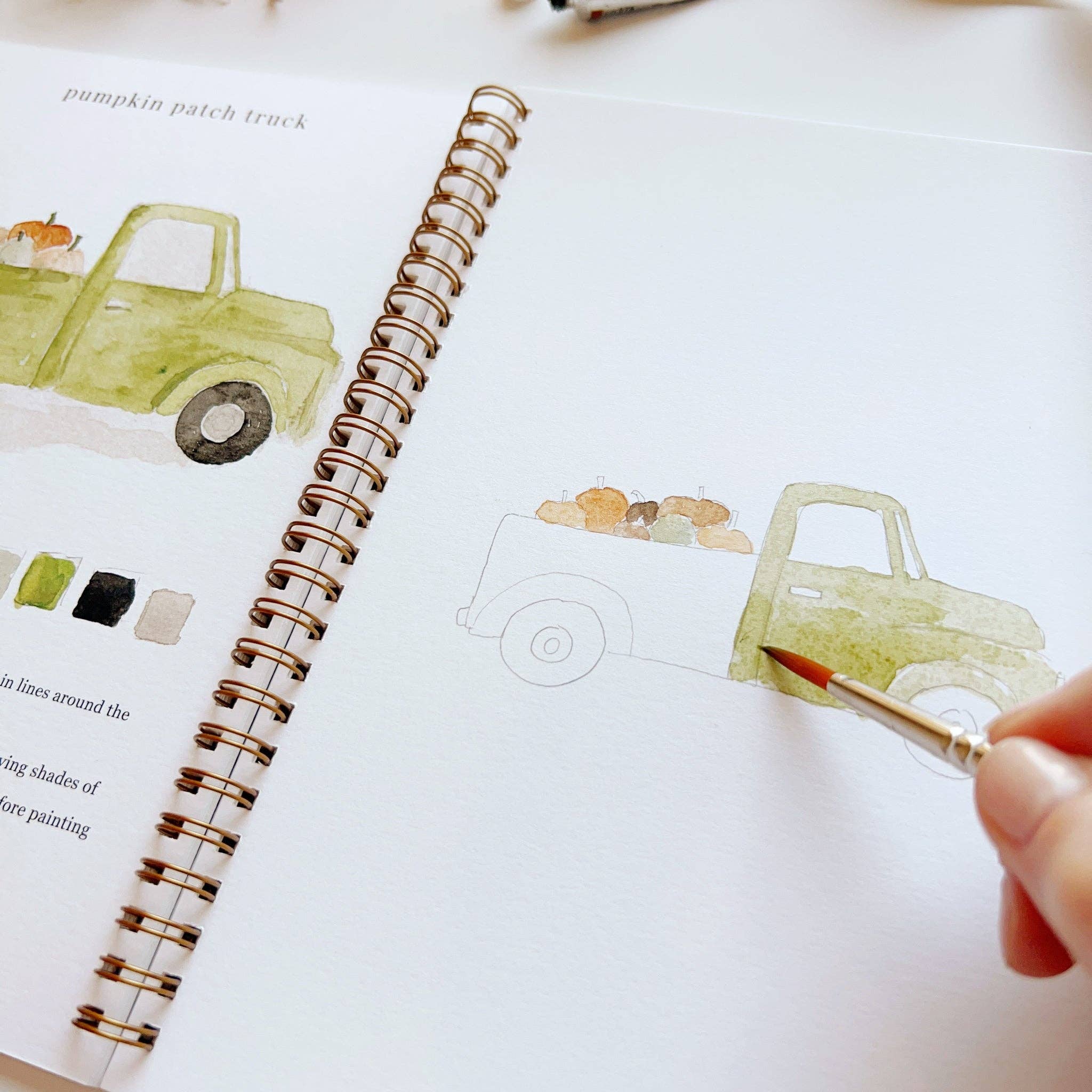 Person painting a watercolor truck on a notebook with a brush