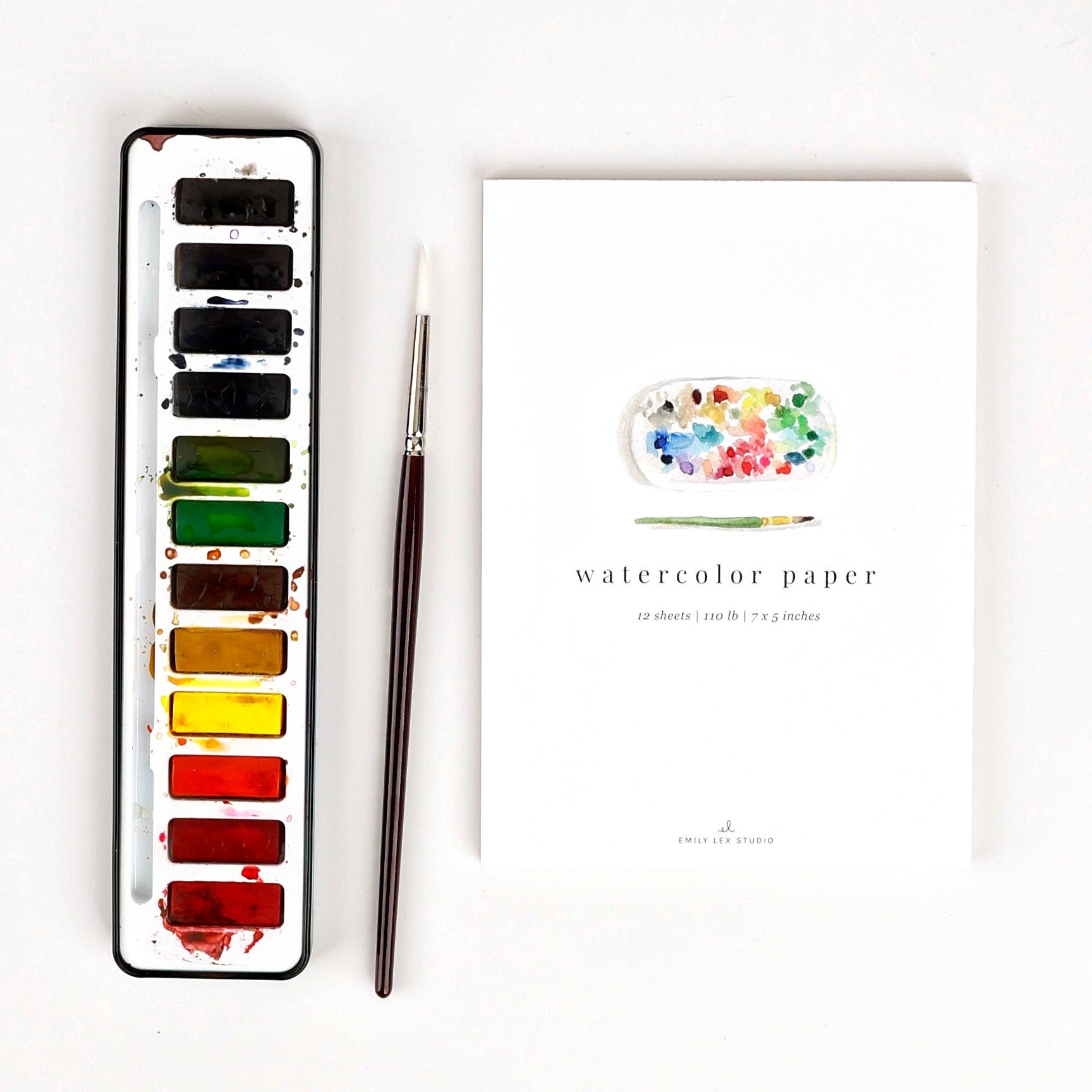 Watercolor set with paint pan, brush, and watercolor paper on a white background