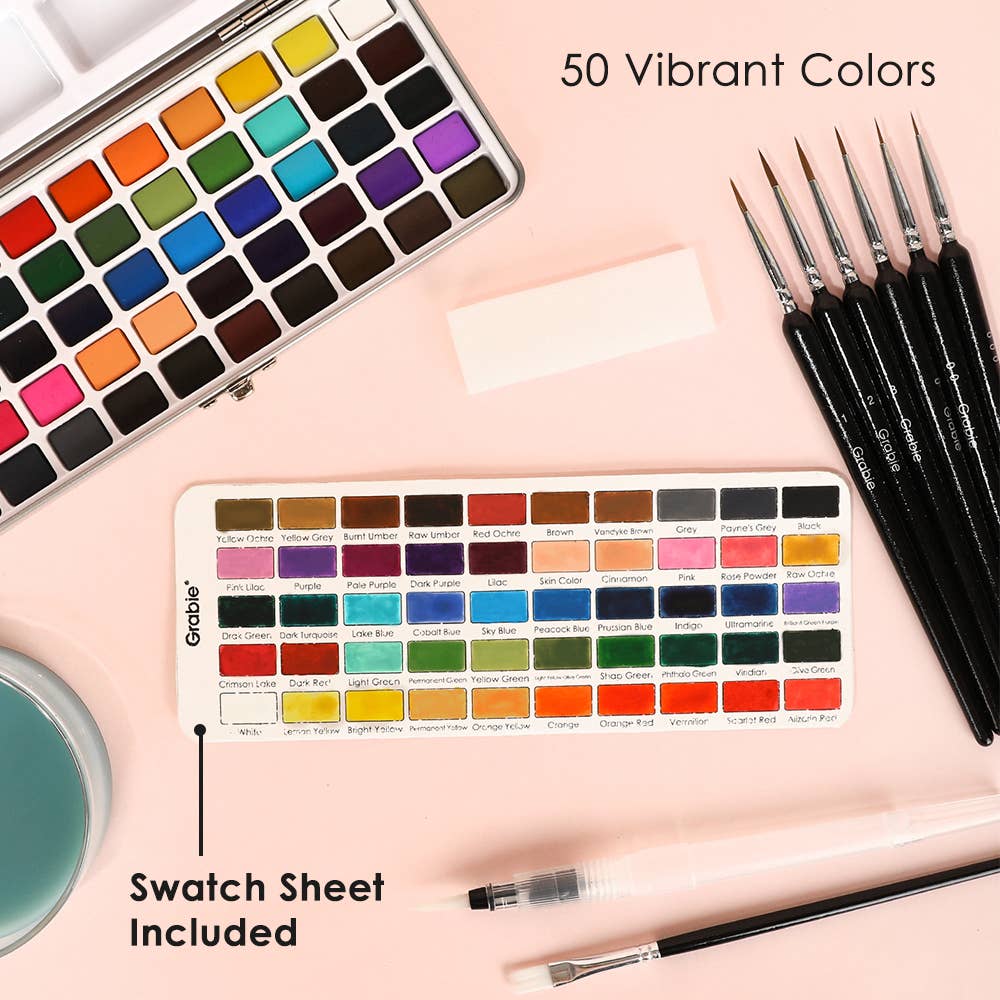 Set of watercolor paints with a swatch sheet and brushes on a pink background