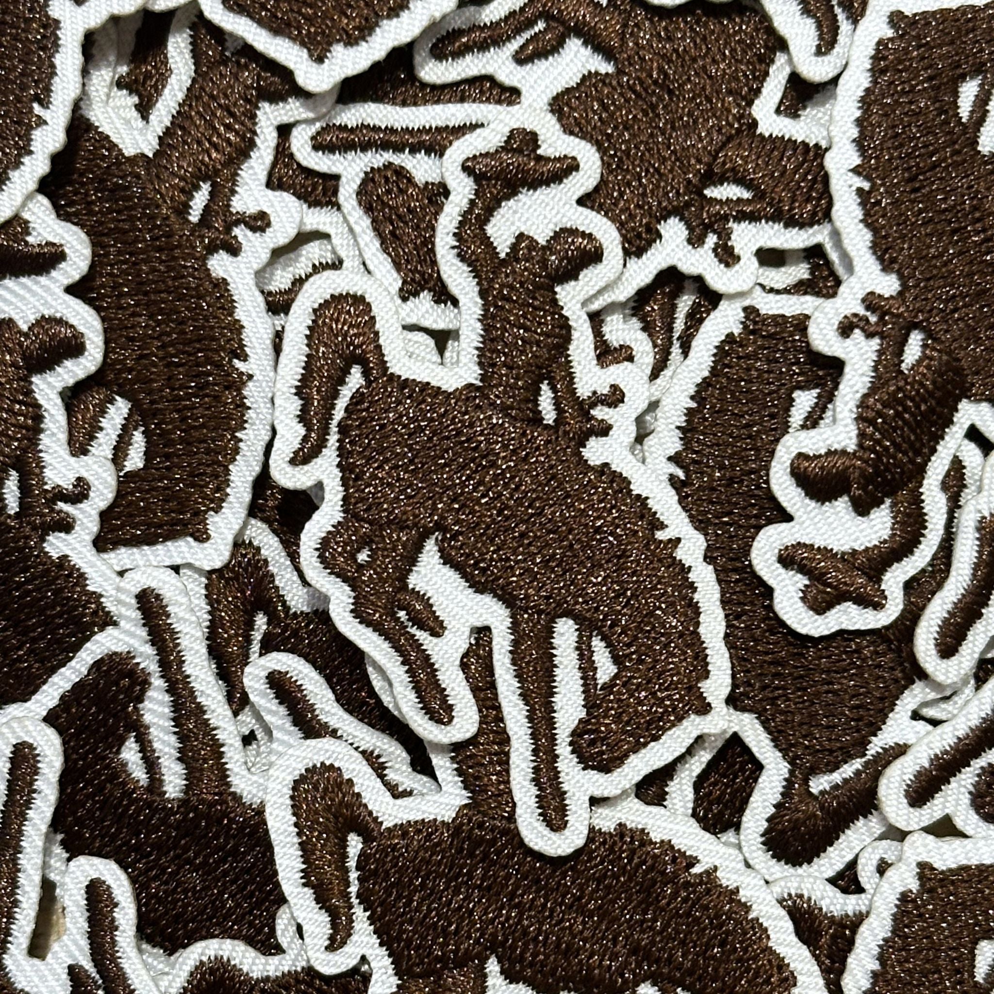 Embroidered patch, showing the silhouette of a bucking bronco and cowboy in brown stitching and white boarder.