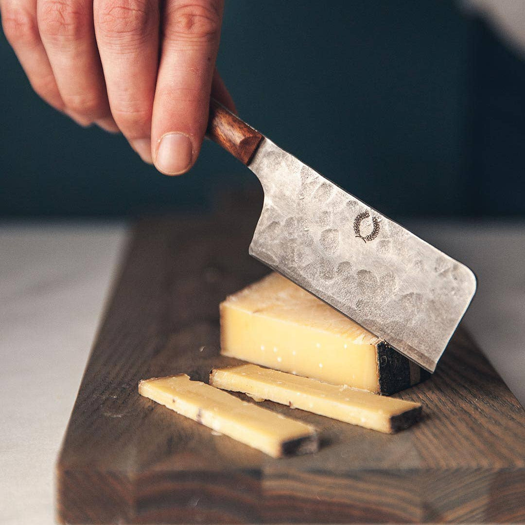 Hand using a cleaver to slice cheese on a wooden board