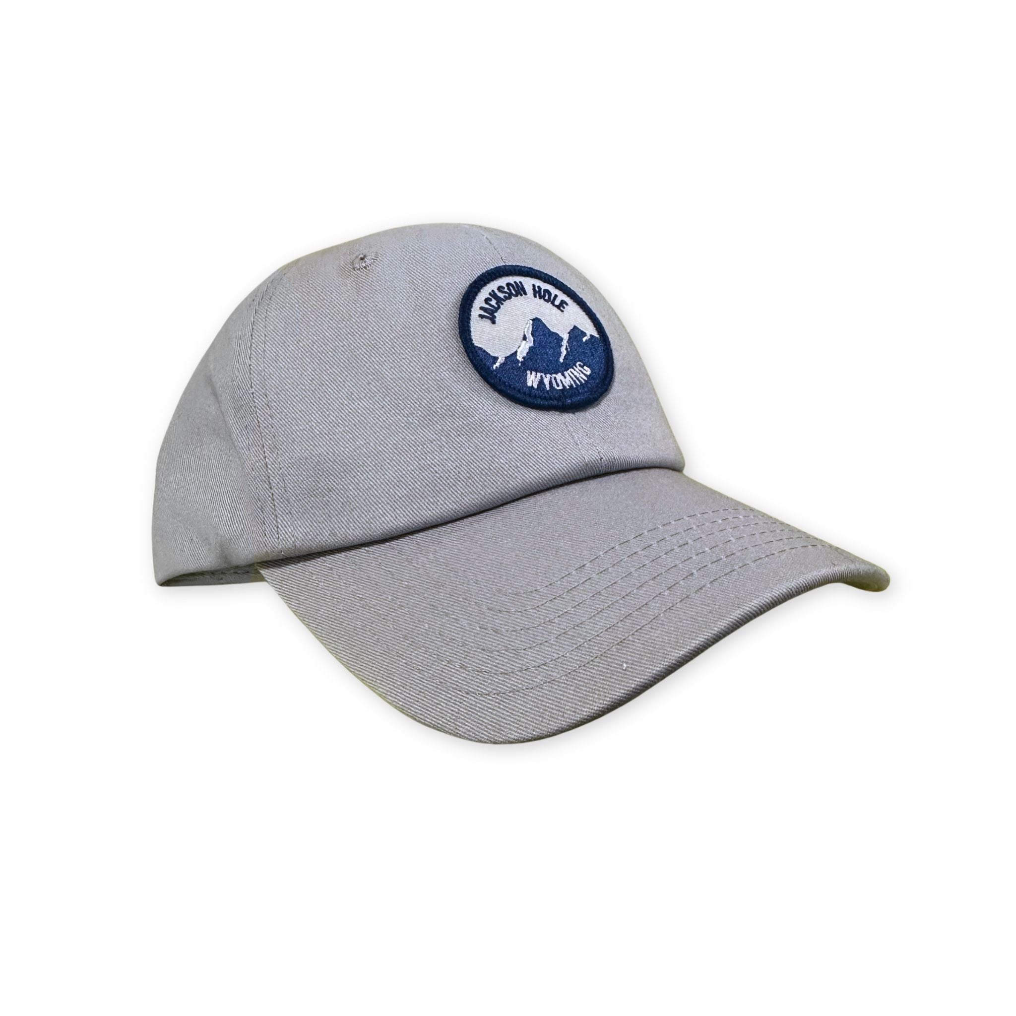 Grey dad hat, with a blue and white round patch that features the mountains and text stating "Jackson Hole Wyoming"