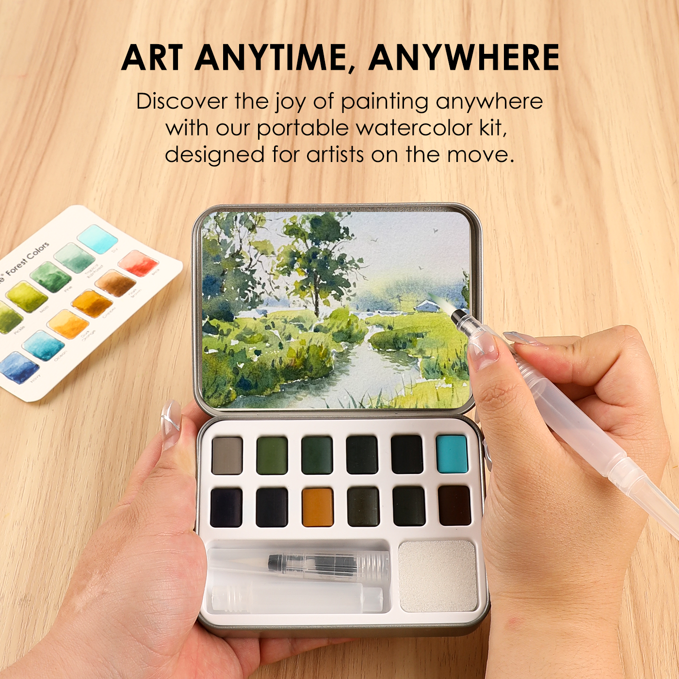 Portable watercolor kit with paint swatches and a hand holding a brush on a wooden surface.