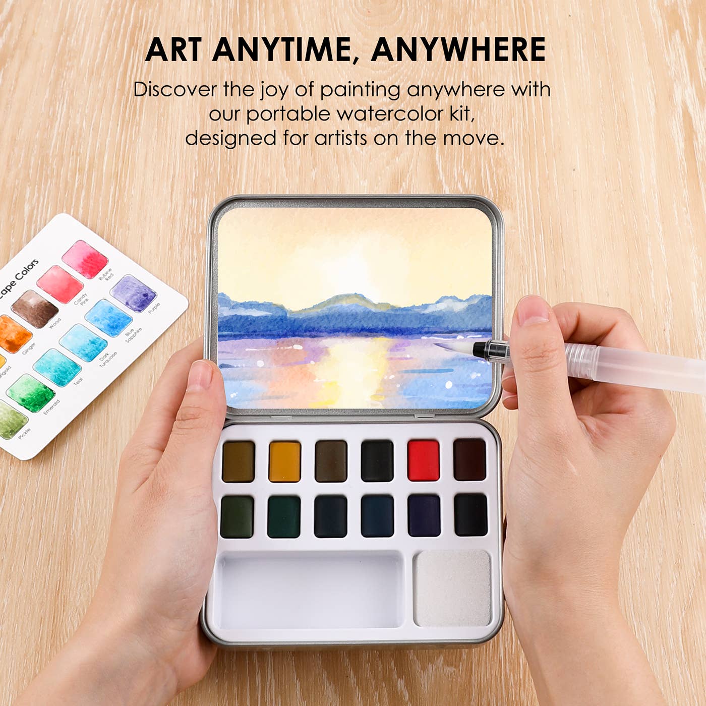 Portable watercolor kit with paint swatches and a scenic painting on a wooden surface.