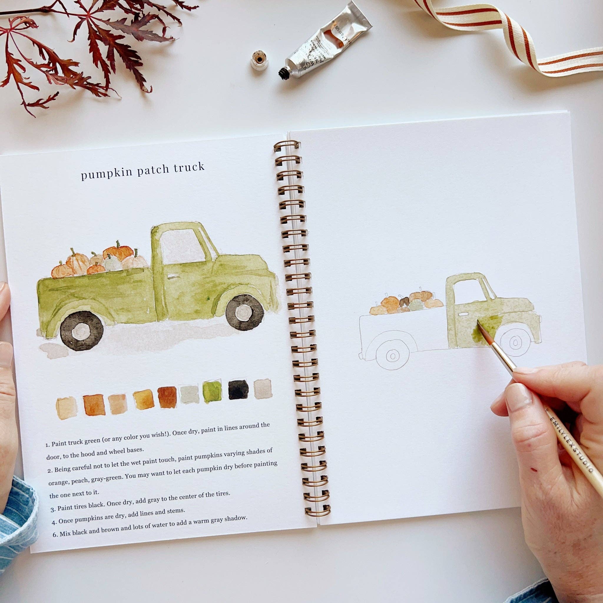 Artbook with a green truck illustration and color swatches, held open by a hand with a paintbrush.
